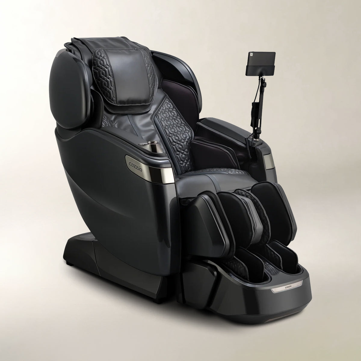 A black modern massage chair with a foot rest, quilted patterned details, and an adjustable arm-mounted screen, photographed on a neutral light beige studio background.