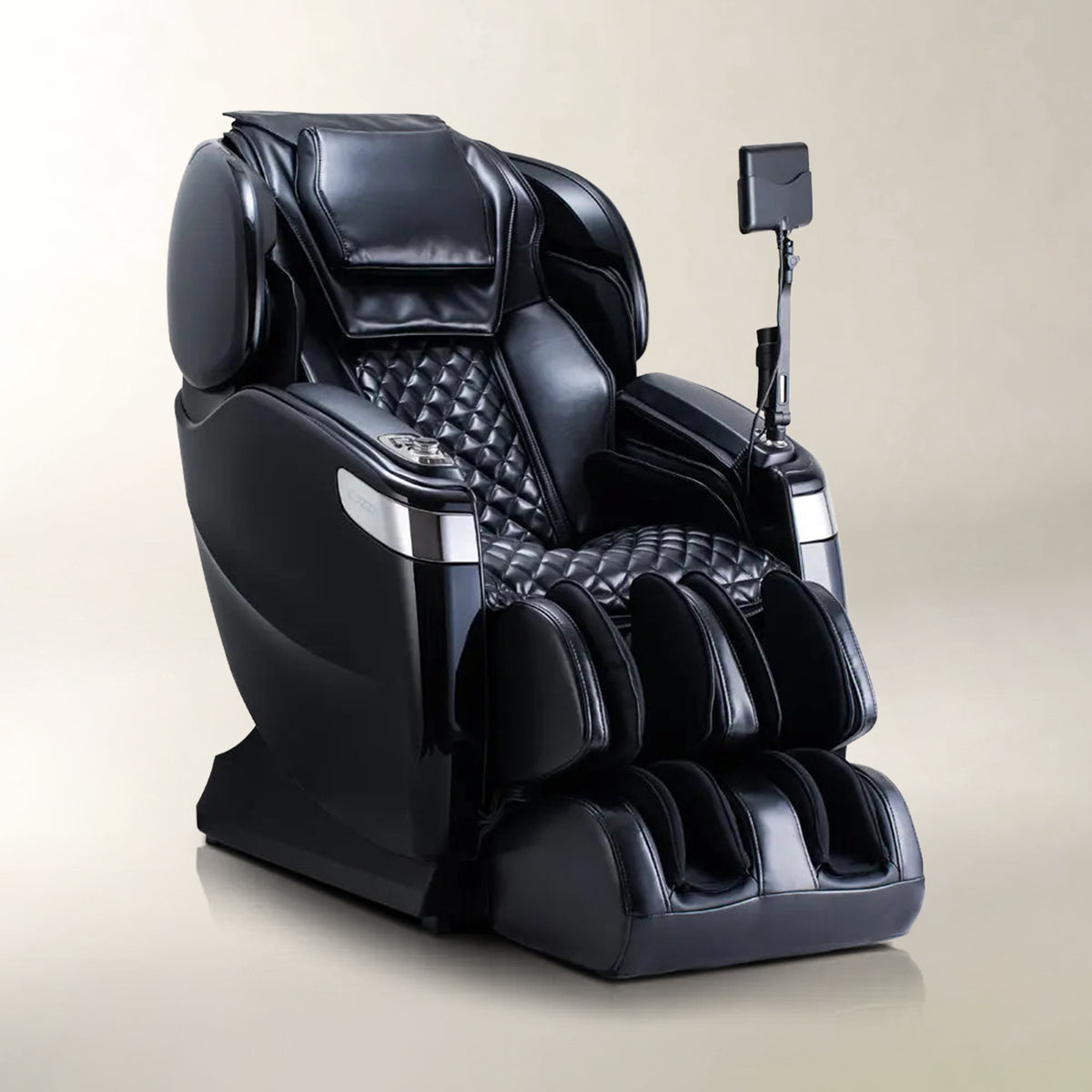 A black massage chair with quilted stitching, a foot massager base, and an adjustable armrest holding a small rectangular device, shown on a plain beige studio background.