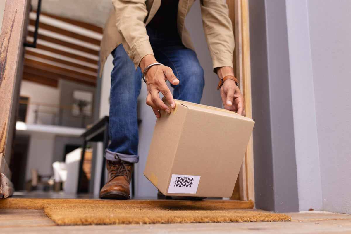 Person picking up a delivered cardboard package from their doorstep.
