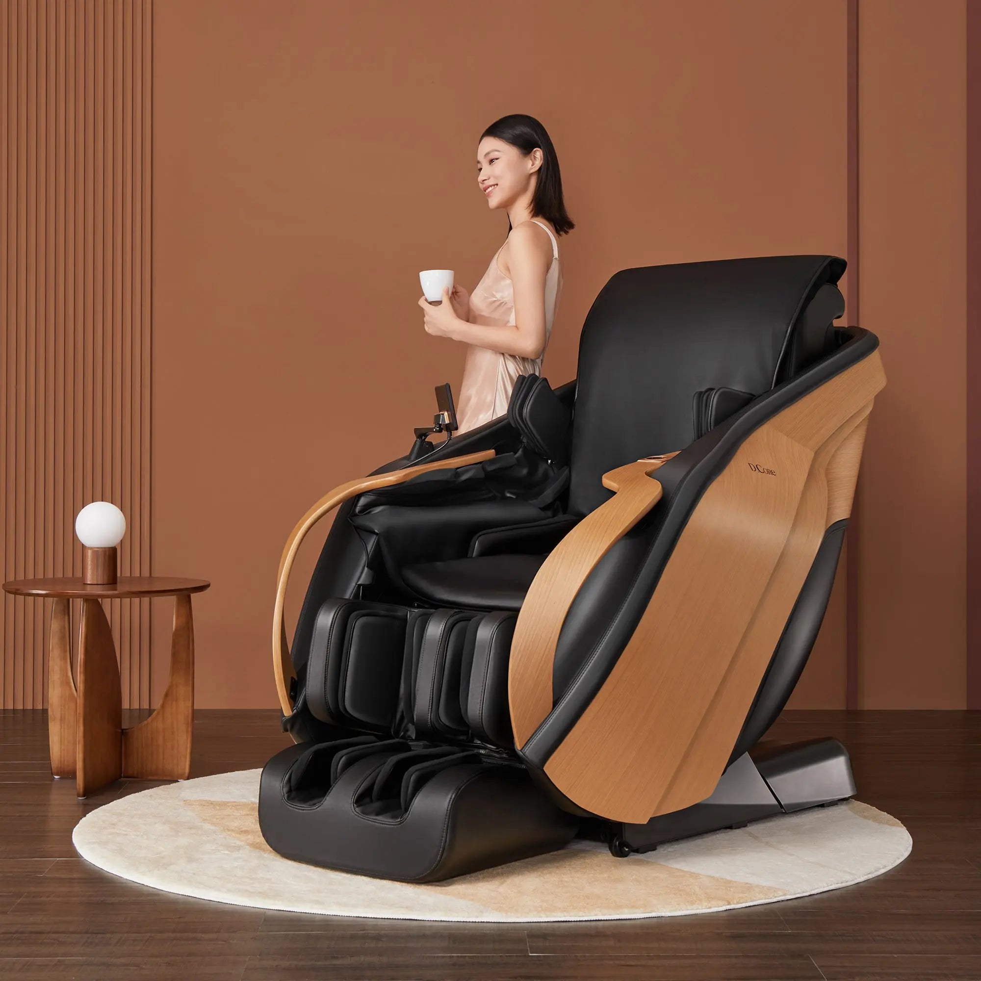 Woman sitting in a modern massage chair holding a cup in a room with a brown wall.