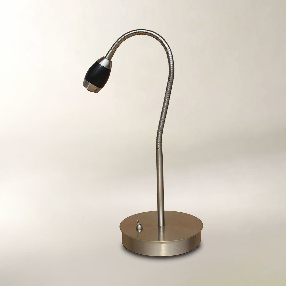 A modern desk lamp with a flexible metallic gooseneck arm, a round brushed metal base, and a black bulb housing, shown against a plain light beige background.