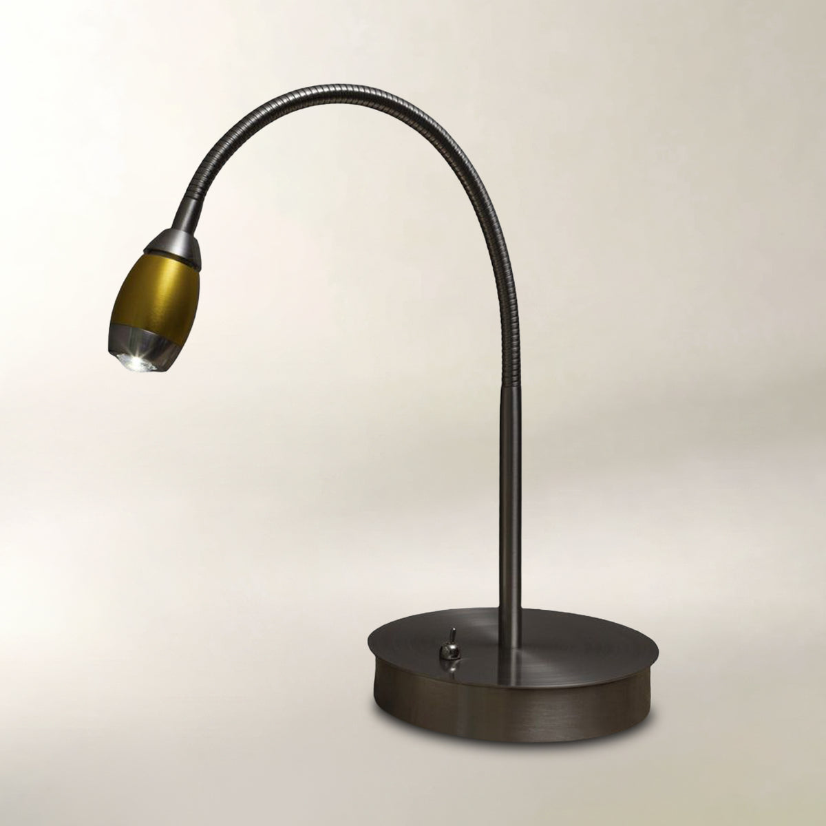A modern gooseneck desk lamp with a matte black flexible arm and a round base, featuring a metallic gold shade, set against a plain light beige background.