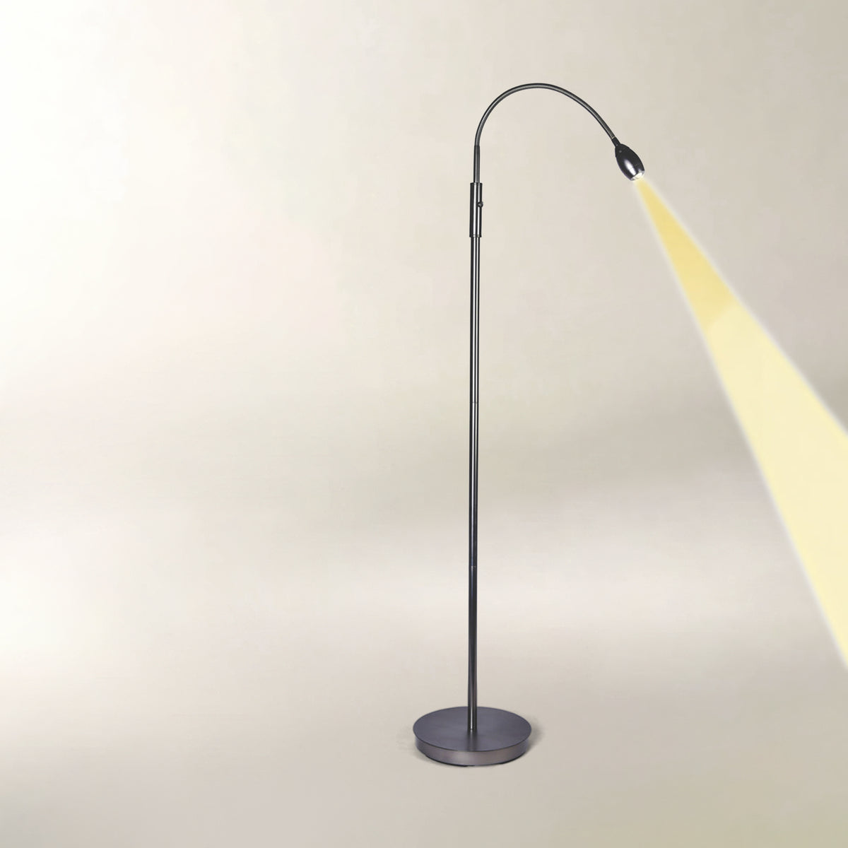 A modern adjustable floor lamp with a dark gray metal stand and flexible gooseneck arm, shown casting a warm yellow light beam against a plain beige background.
