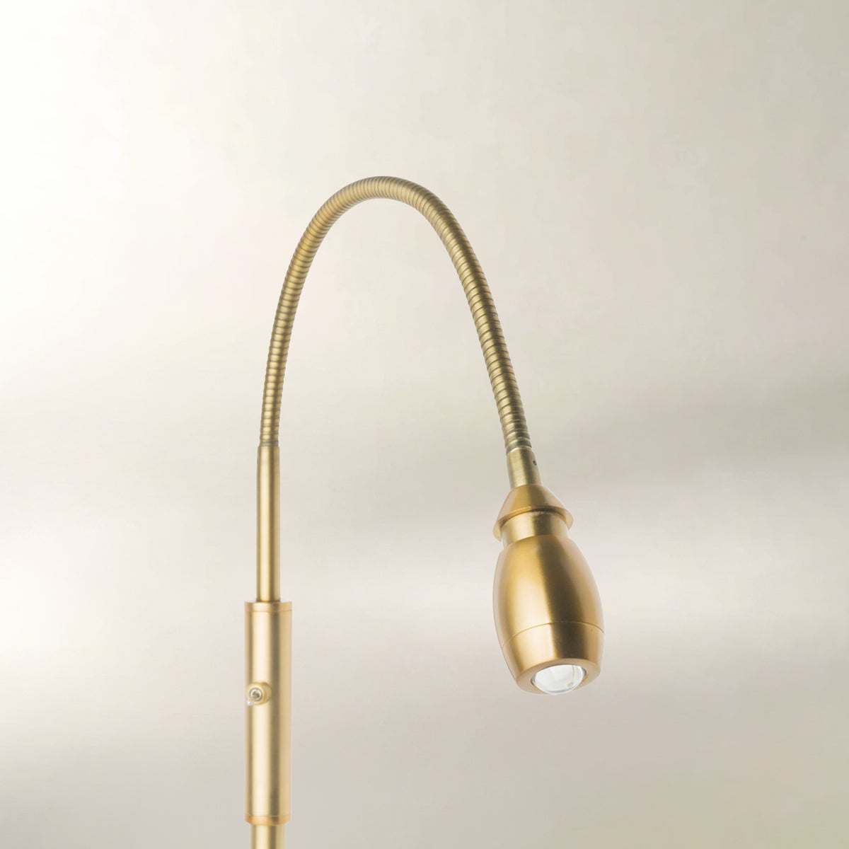 A modern adjustable gooseneck desk lamp in a brushed brass or gold finish, shown against a plain light beige background.
