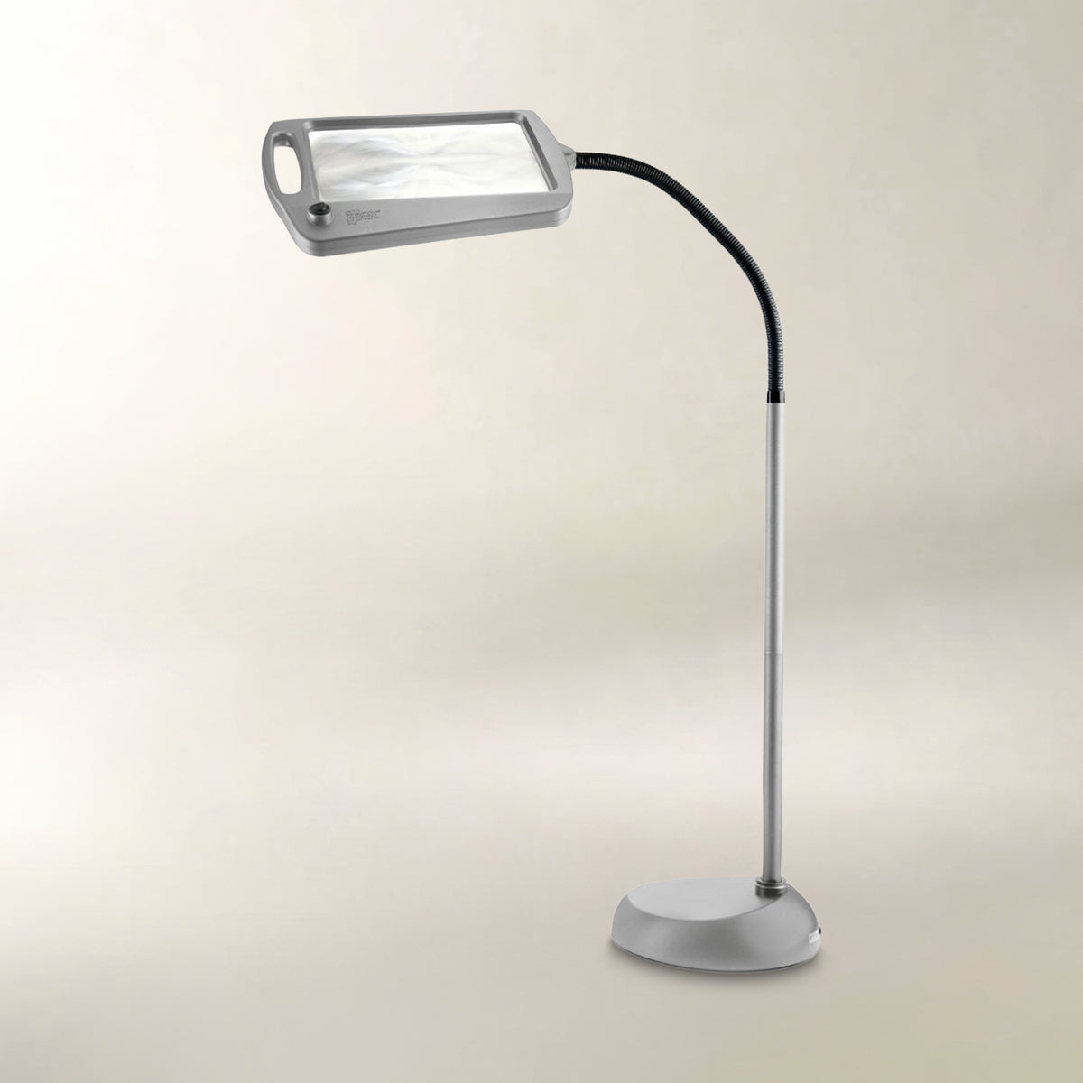 A modern magnifying lamp with a silver metal stand, flexible black arm, and rectangular magnifying head, shown against a plain beige background.