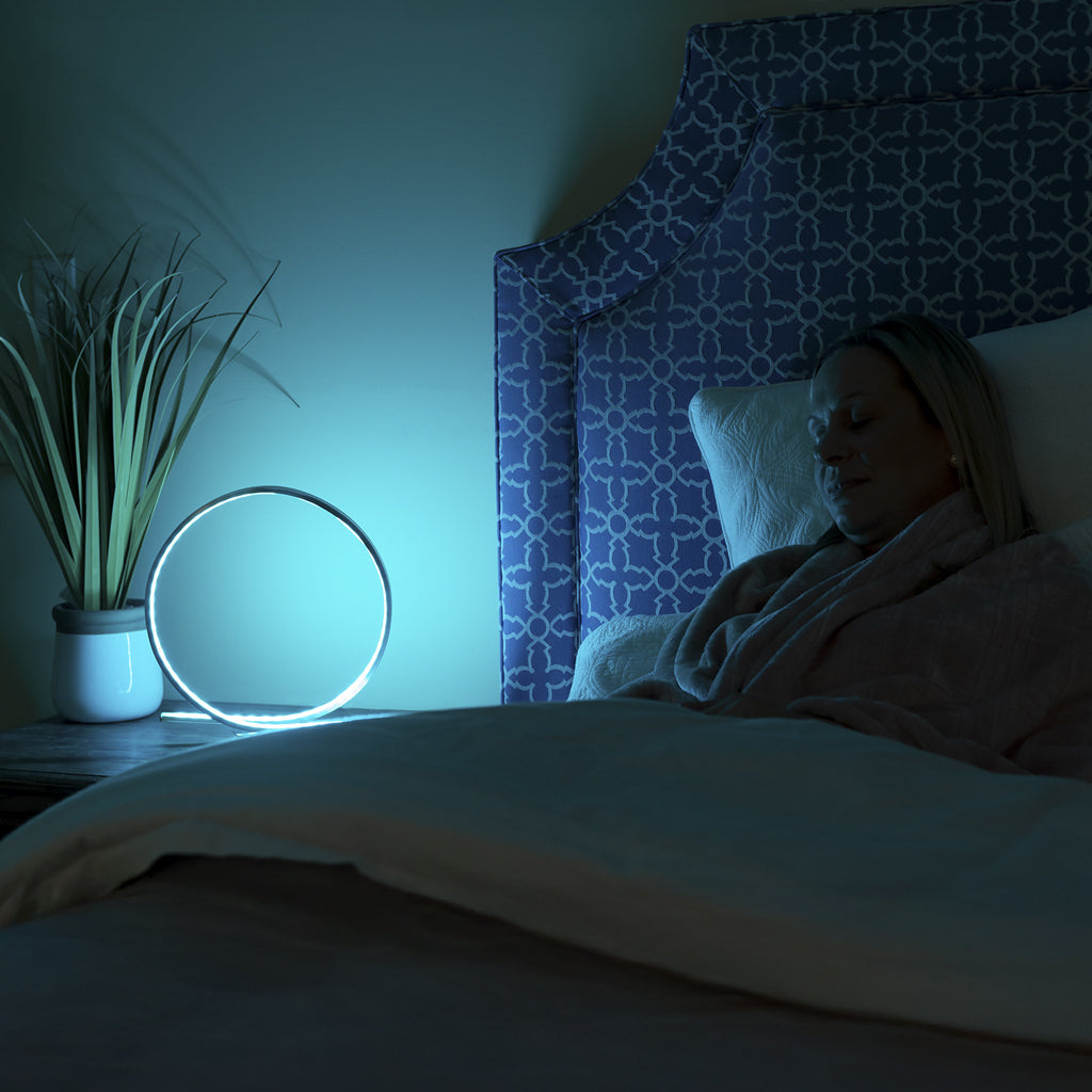 Person lying in bed under a blanket with a night light on a nightstand.