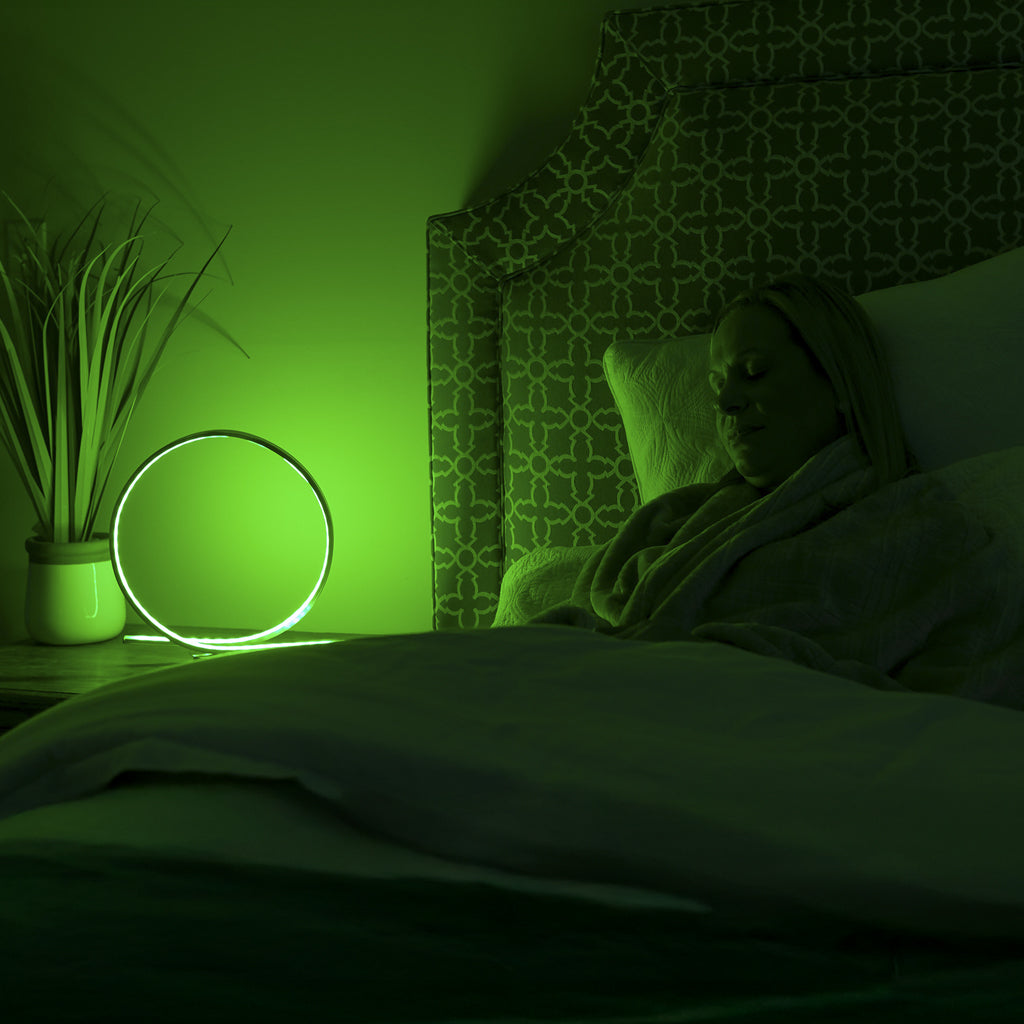 Person lying in bed under a blanket with a green light illuminating the room.