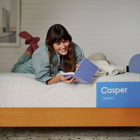 Woman using a laptop on a Casper mattress with a Casper box in the foreground.
