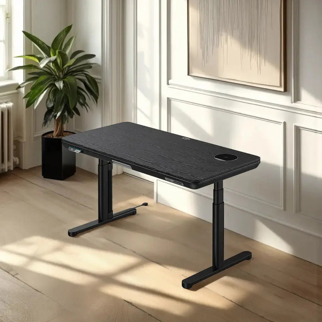 A modern black standing desk with a sleek glass surface sits in a sunlit room with white paneling, a window and a large plant in the corner.