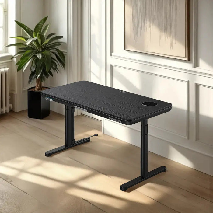 A modern black standing desk with a sleek glass surface sits in a sunlit room with white paneling, a window and a large plant in the corner.