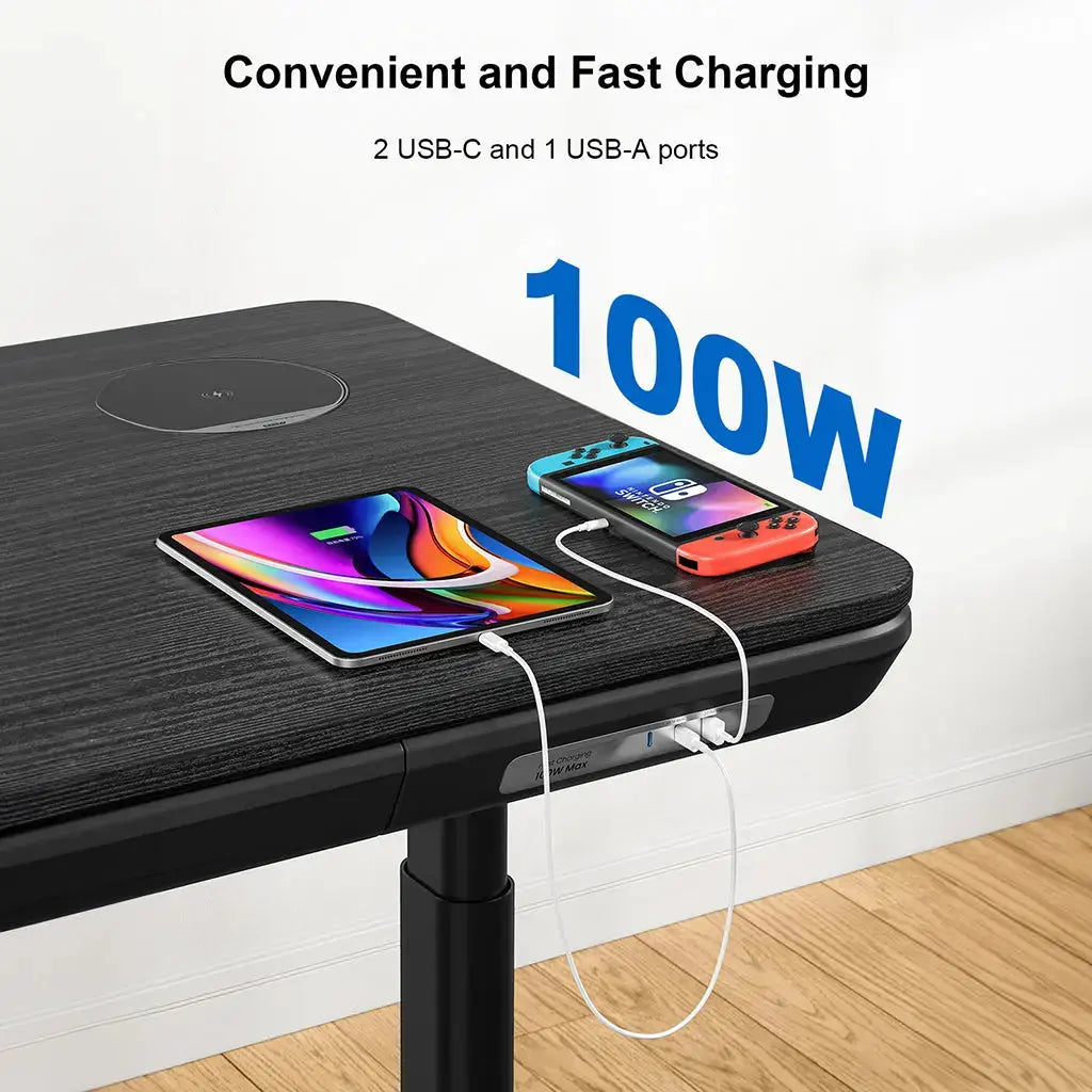 Close-up of a black standing desk charging a tablet and gaming device via built-in USB ports.