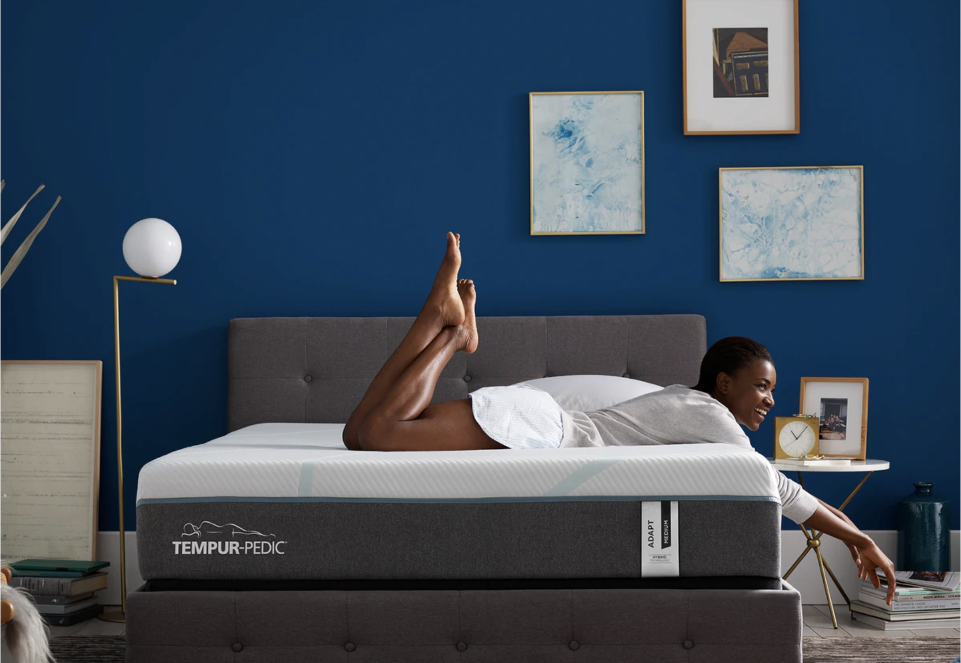 A lady on the TEMPUR-ADAPT® 11" MEDIUM HYBRID MATTRESS in a furnished bedroom