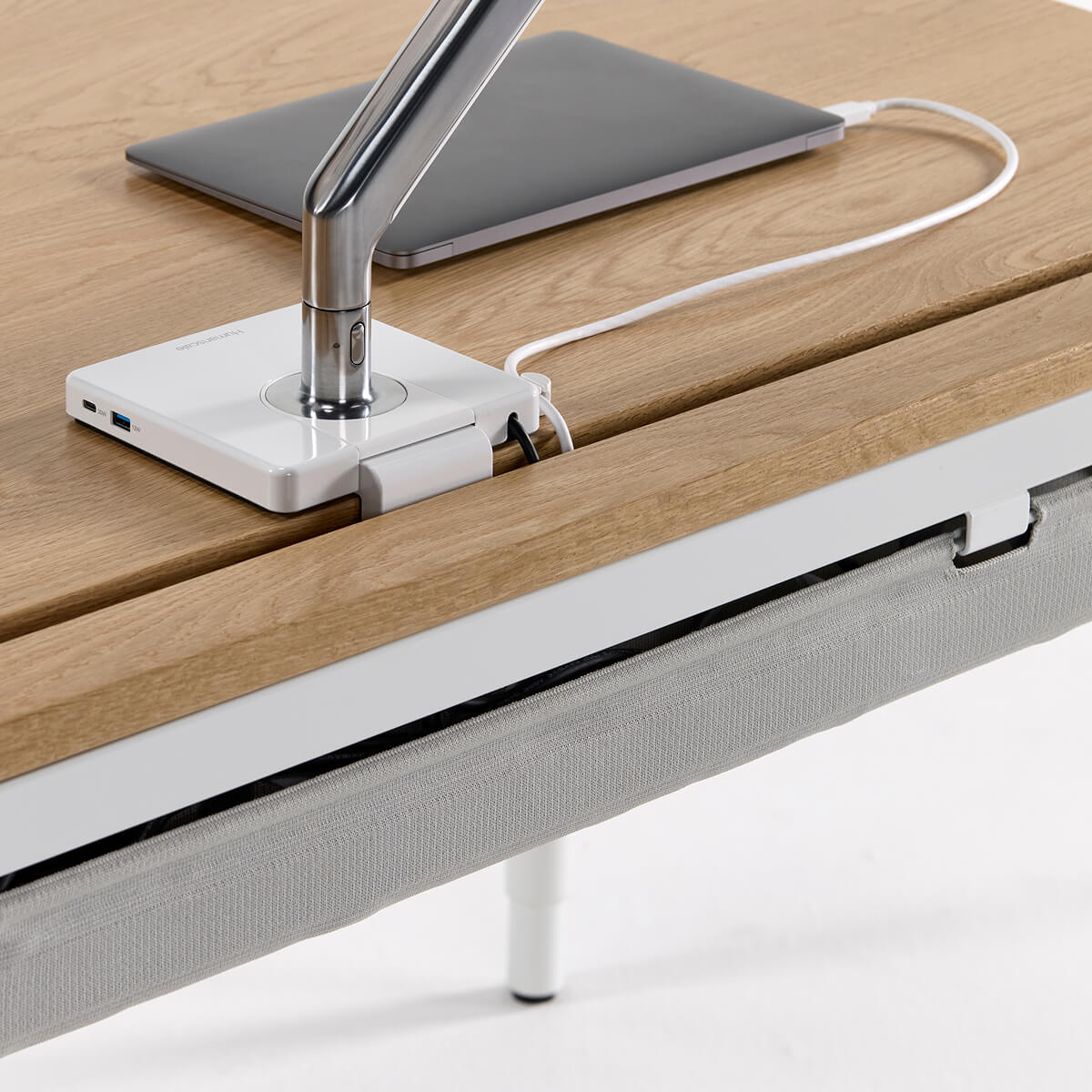 Close-up of a modern desk with a laptop, lamp, and power strip on a wooden surface.