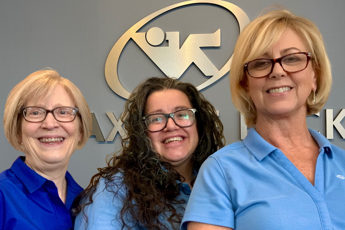 Three women in blue shirts standing in front of a logo on a wall
