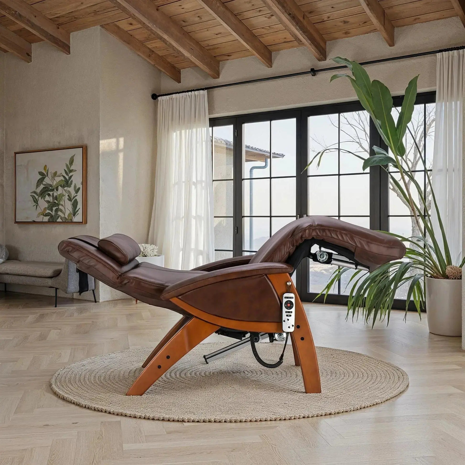 Brown leather zero gravity recliner with wood base positioned in a sunlit room featuring large windows, a round woven rug, and modern natural decor.