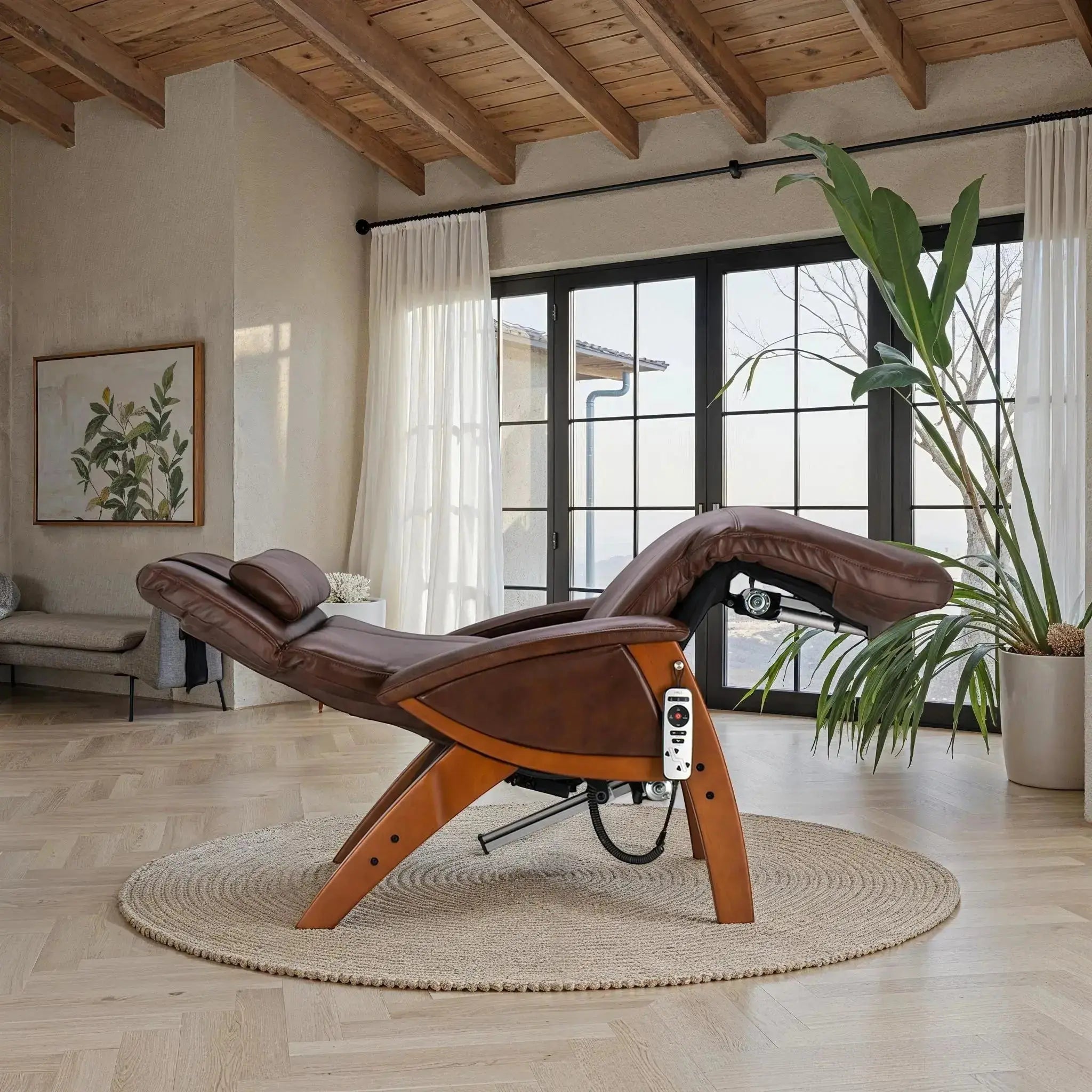 Brown leather zero gravity recliner with wood base positioned in a sunlit room featuring large windows, a round woven rug, and modern natural decor.