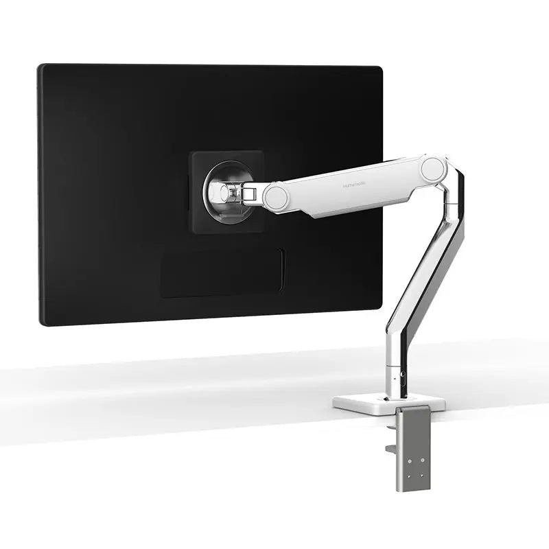 A sleek silver monitor arm is mounted to the edge of a white desk, securely holding a flat-screen monitor in a floating position.