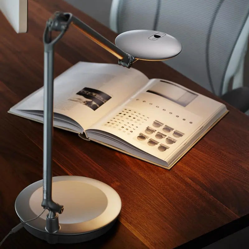 The Humanscale Element Disc Light in silver shown on an office desk.