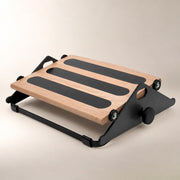 A wooden and black adjustable footrest with three non-slip rubber pads on the slope, shown on a neutral beige background.