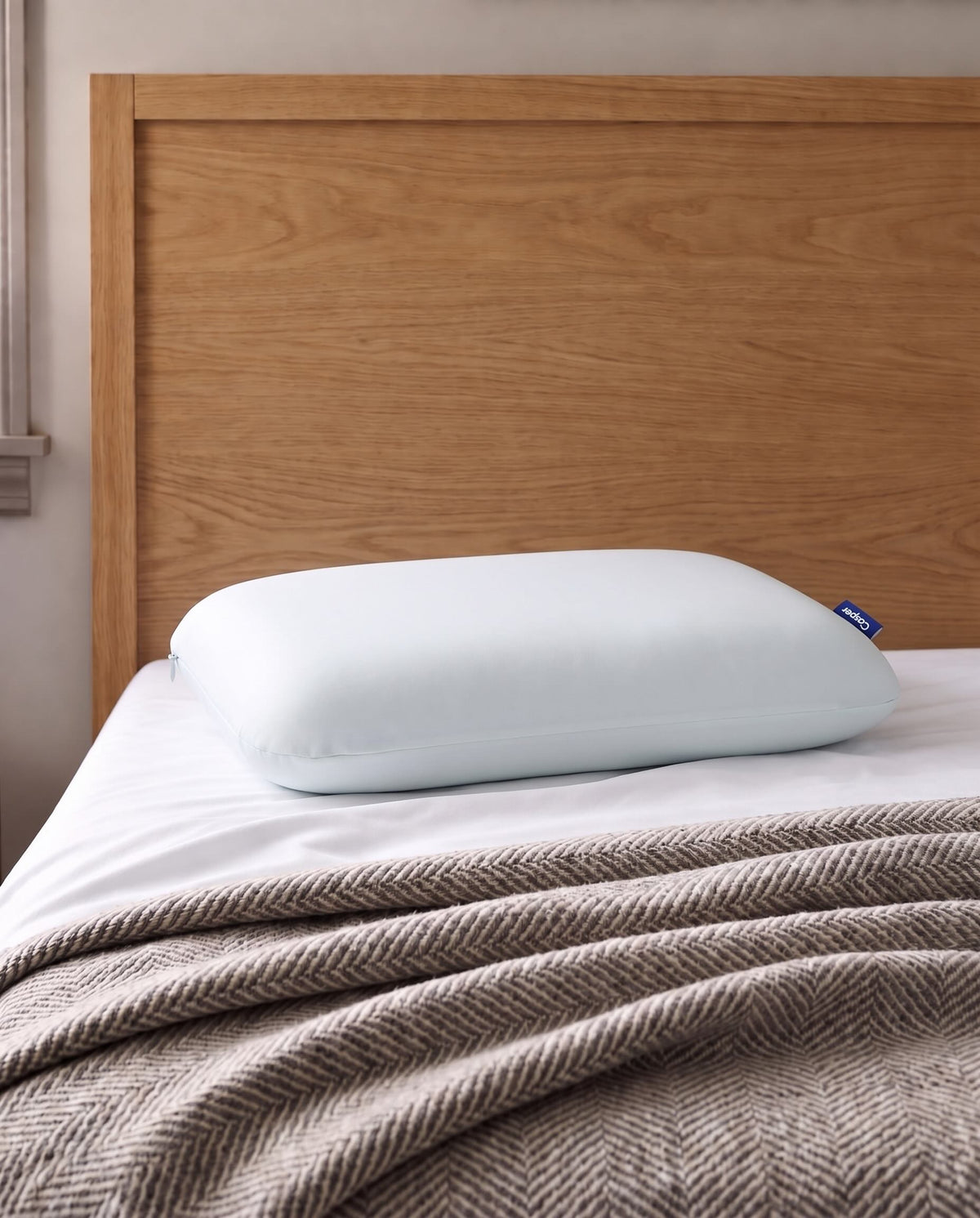 Casper Hybrid Snow King Pillow in white displayed on a bed with a wood headboard and textured blanket.