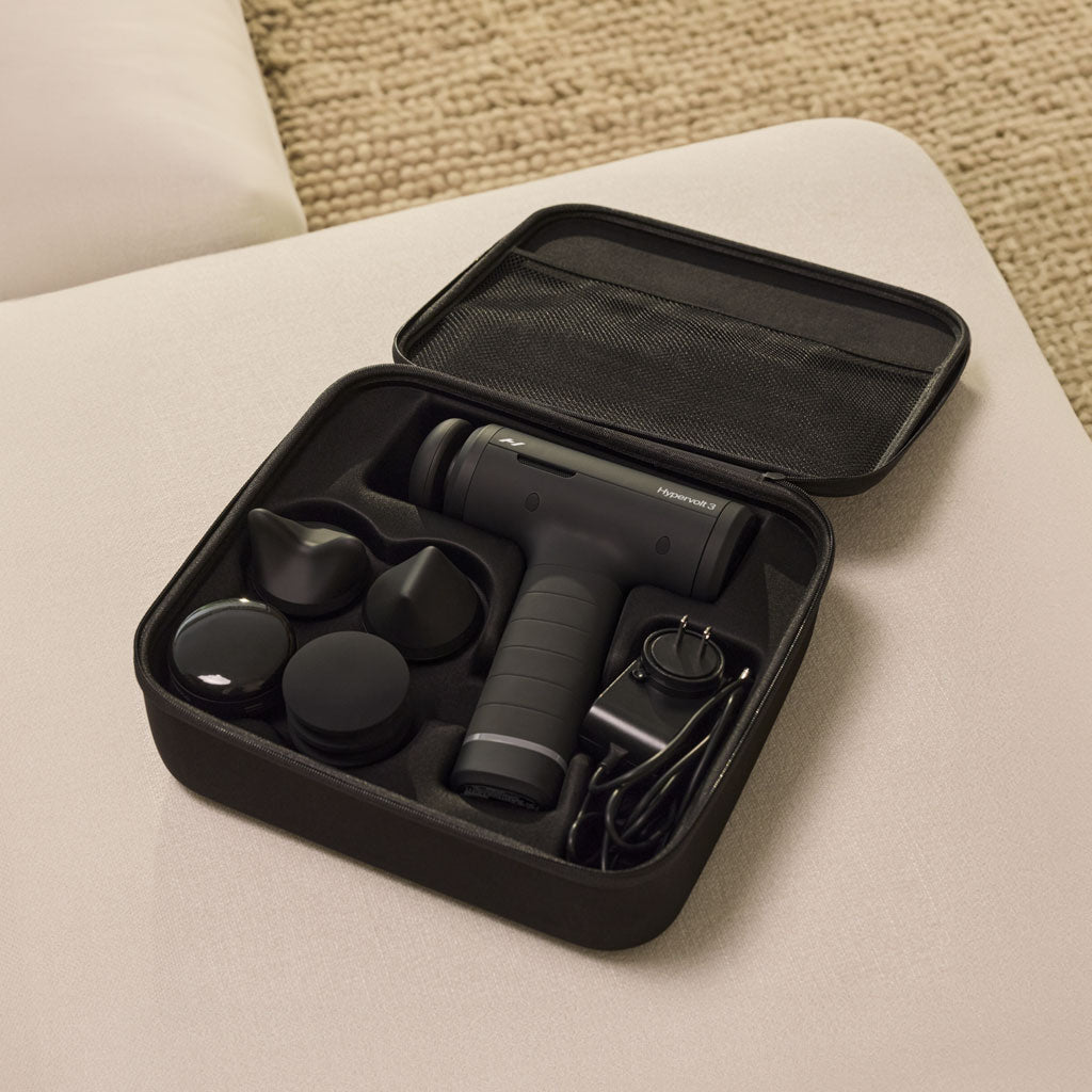 Black handheld massage device with attachments in a black carrying case on a beige surface.