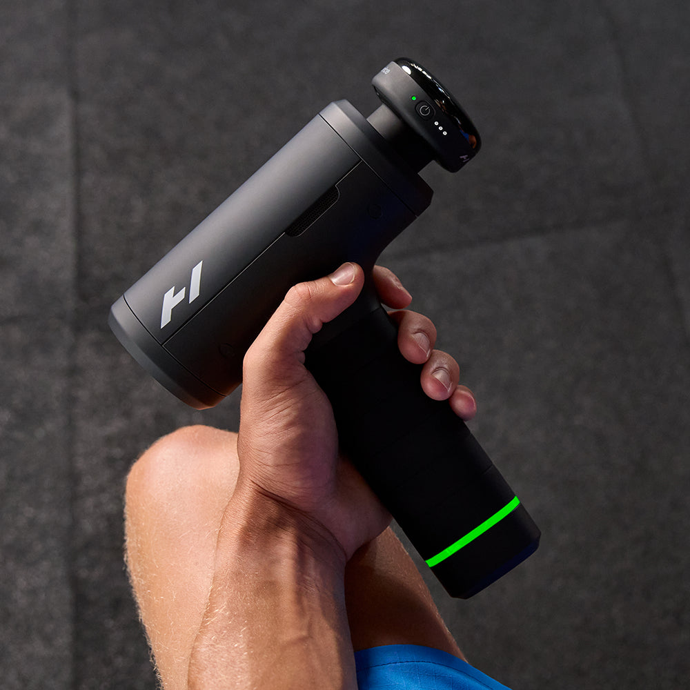 Hand holding a black massage gun with a Hyperice logo against a dark background