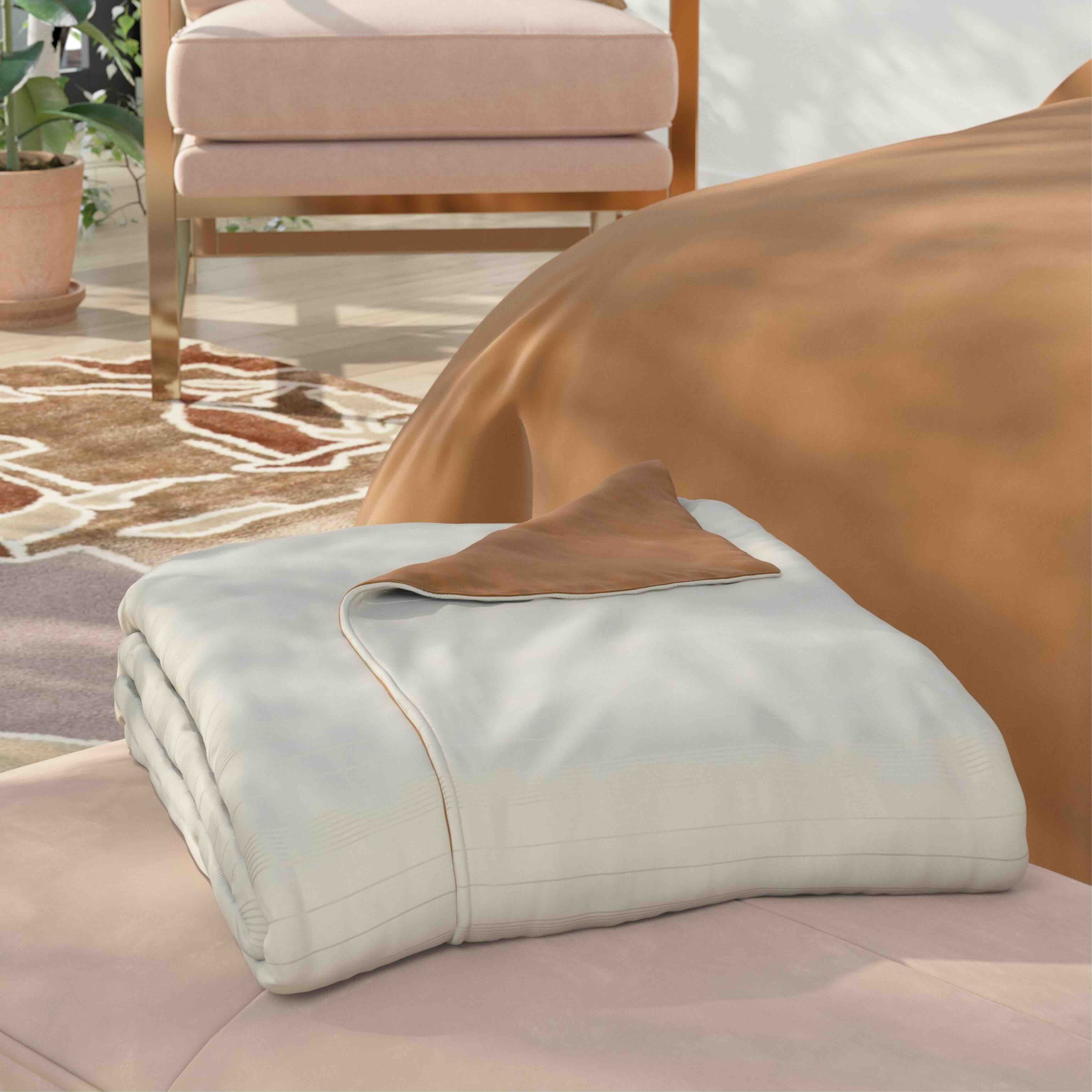 A folded light ivory duver cover with a brown accent, displayed on a pink upholstered bench in a styled bedroom setting.