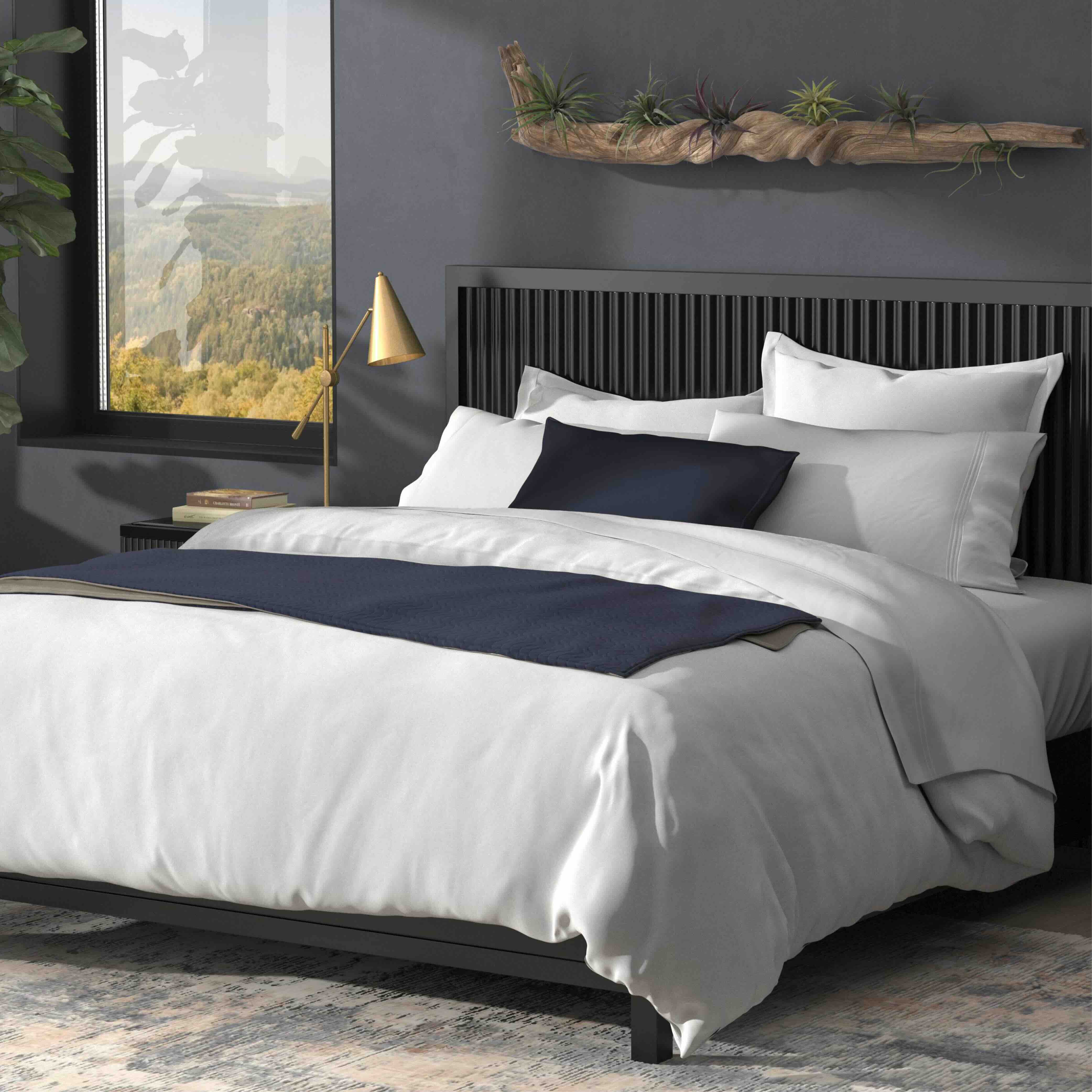 Bedroom with a neatly made bed featuring white and navy bedding, a nightstand with a lamp, and a window with a view.