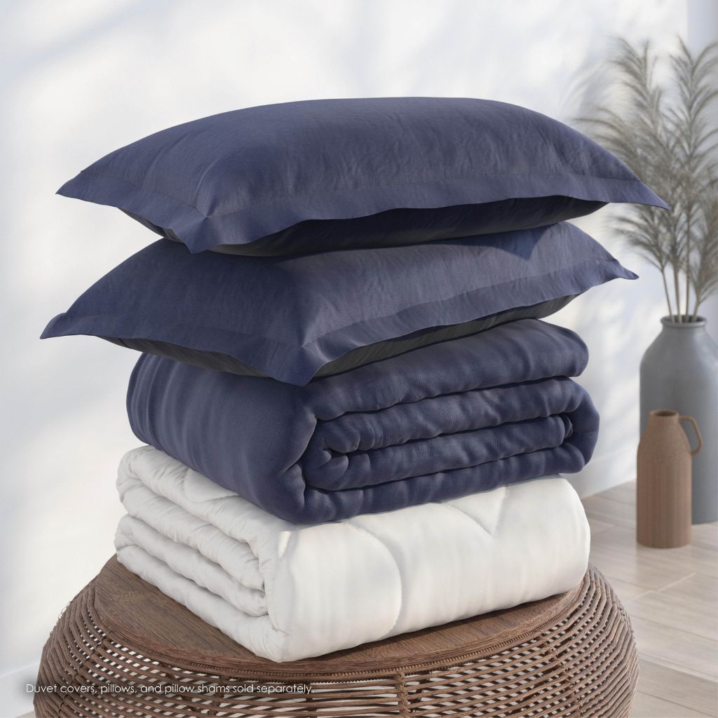 Stack of navy and white bedding on a wicker stool with a neutral background