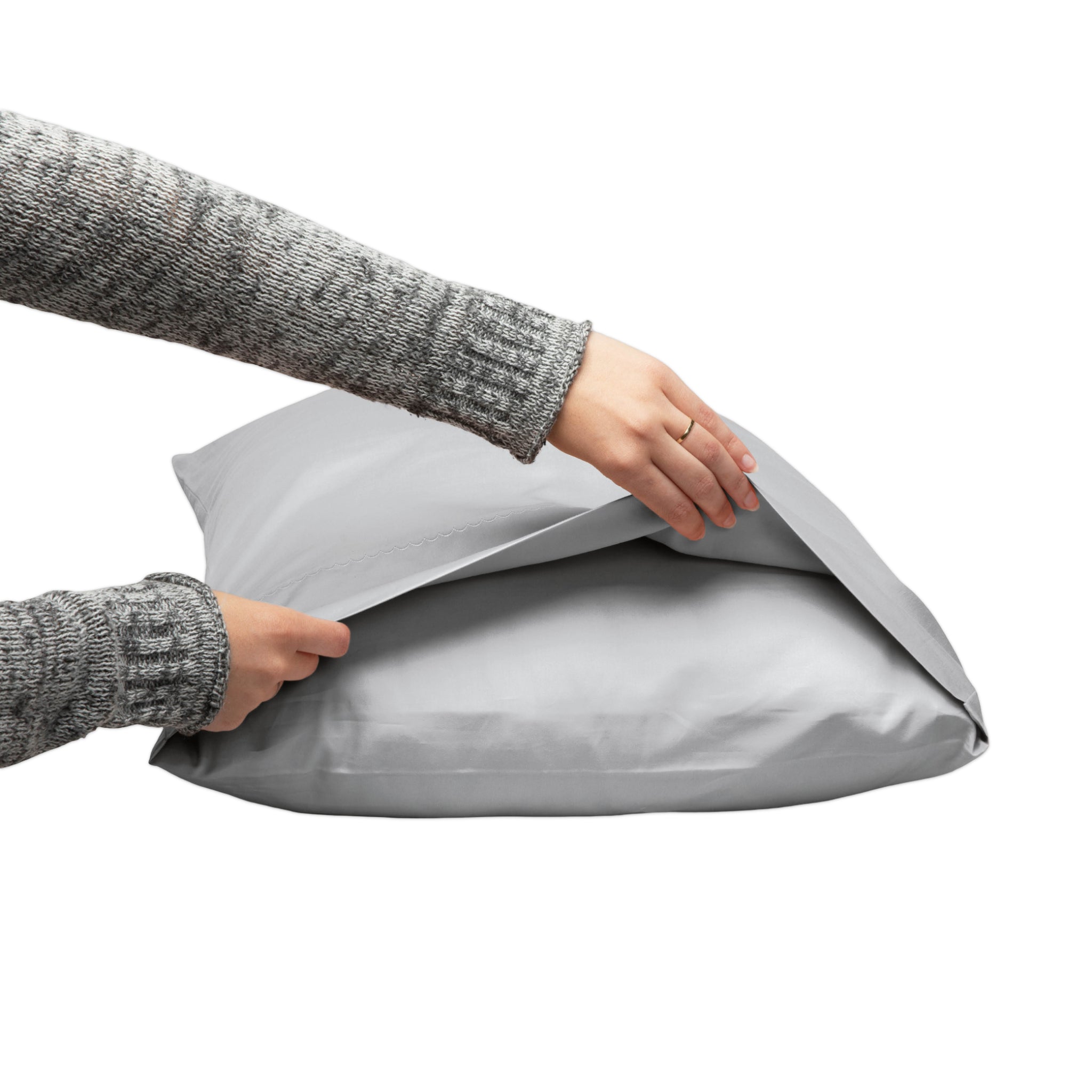 A person wearing a gray knit sweater is shown holding and opening a light gray pillow or cushion against a plain white background.