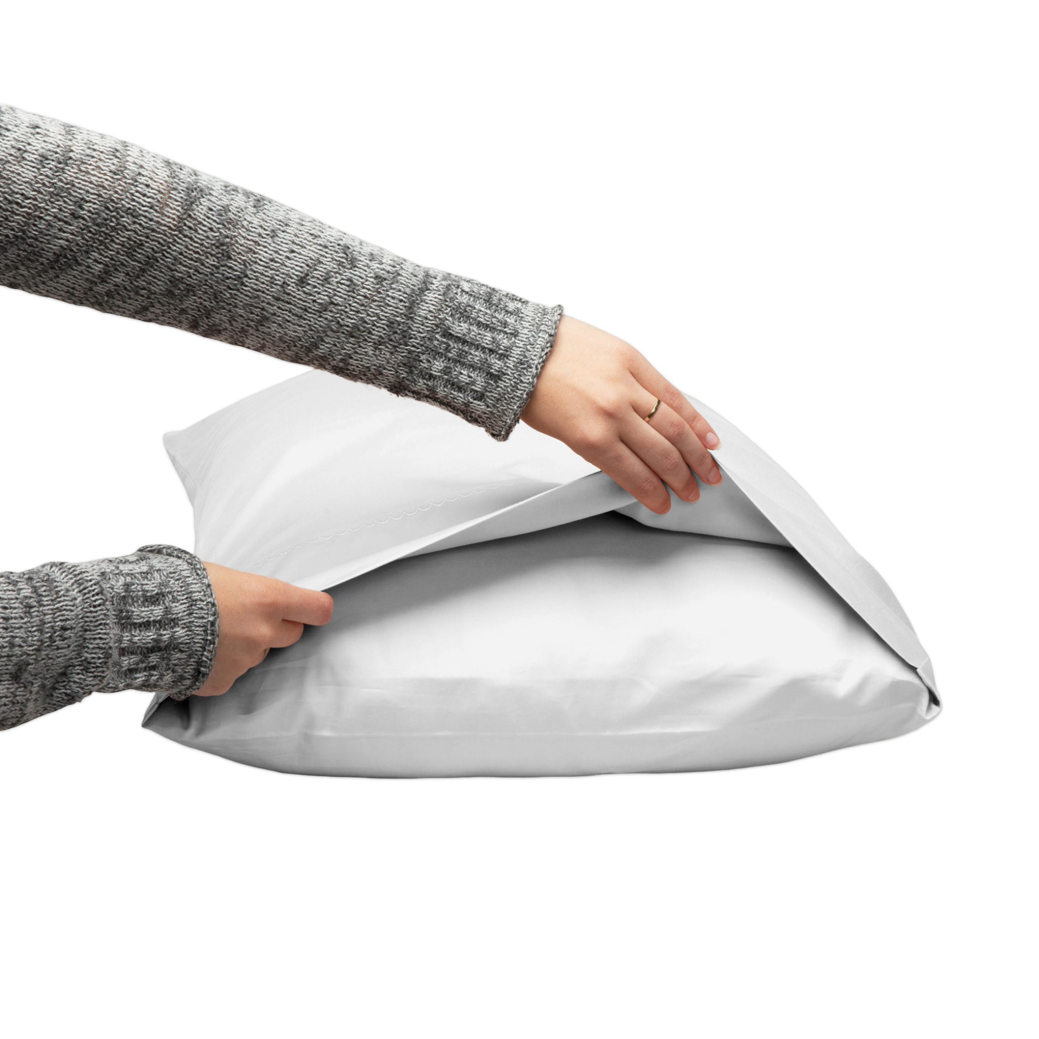 A person wearing a gray knit sweater is shown from the shoulders down, opening a light gray pillowcase with both hands against a plain white background.