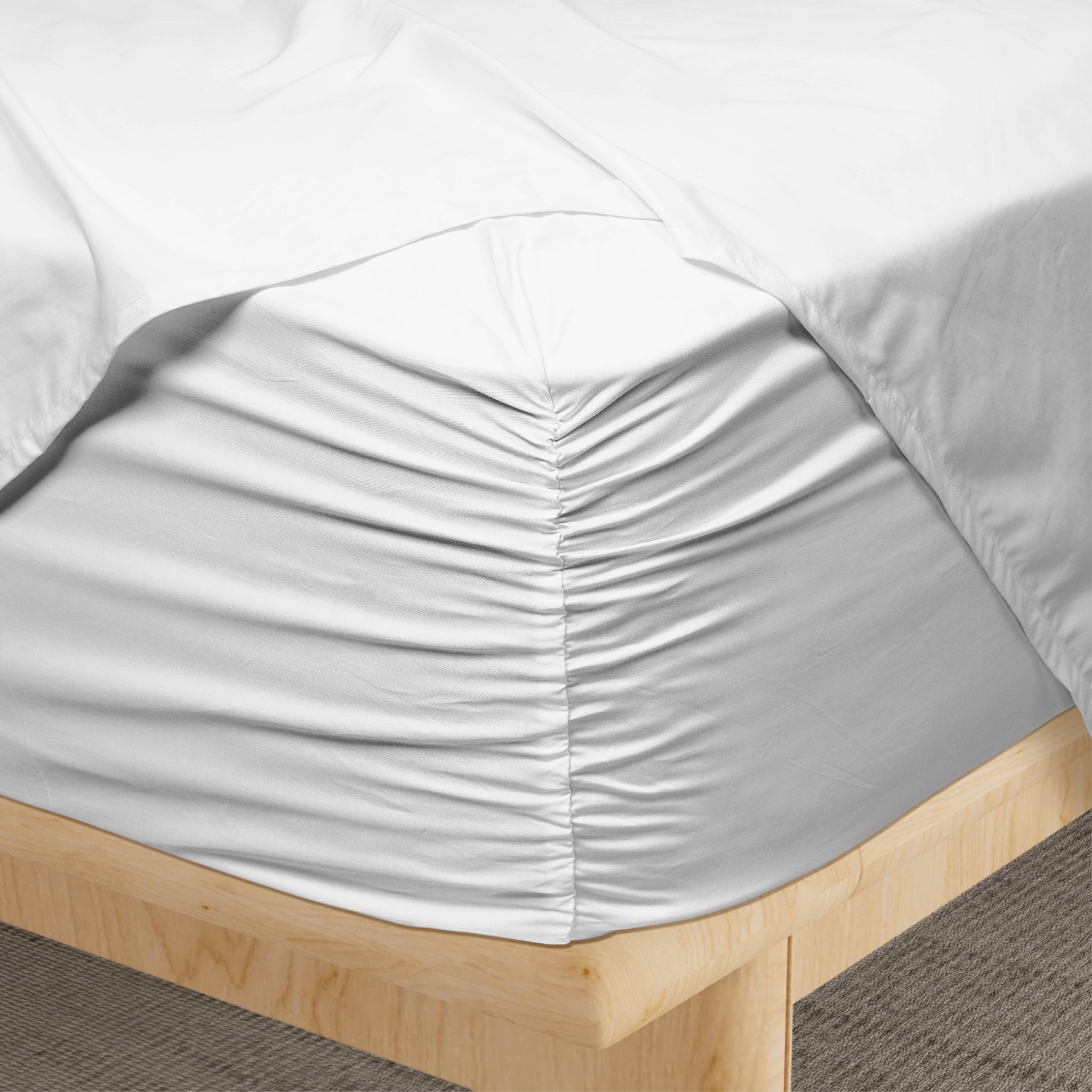 White fitted sheet on a wooden bed frame with gray carpet.