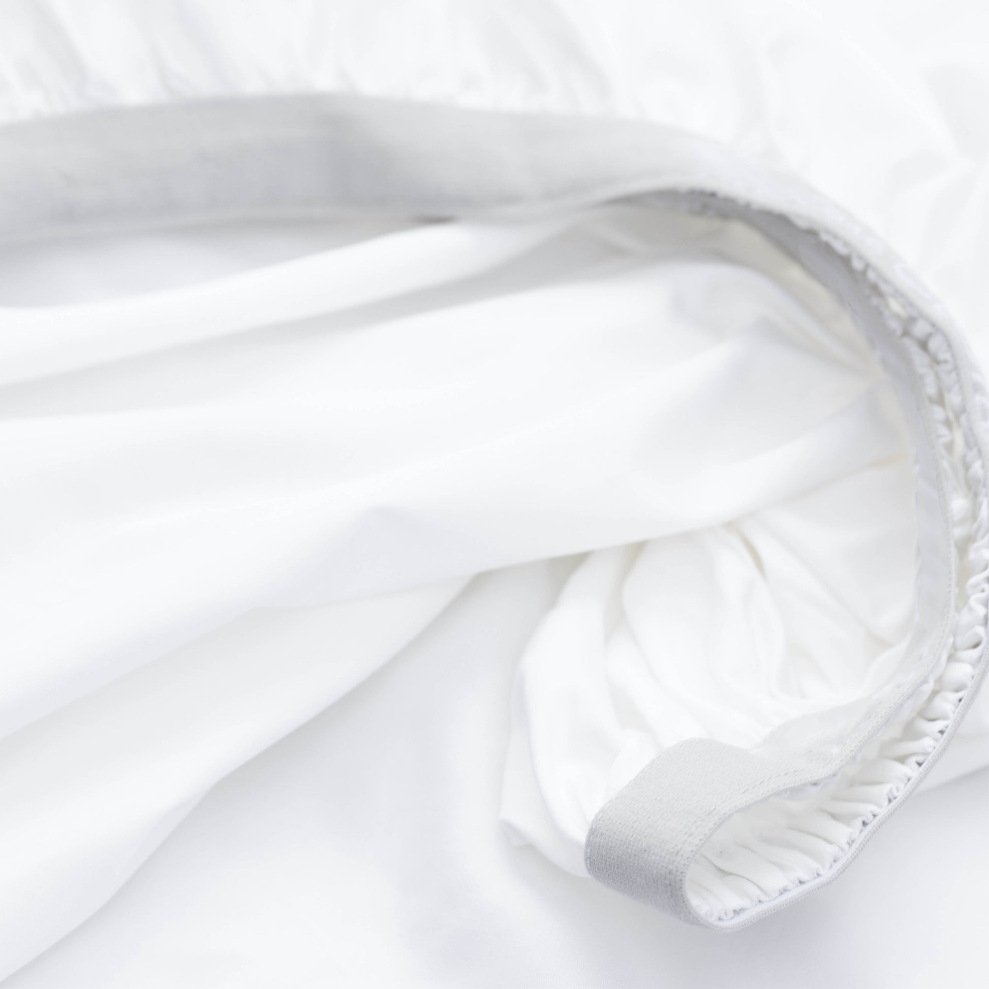 Close-up of a white fitted sheet with a light gray elasticized edge and stitched hem detail.