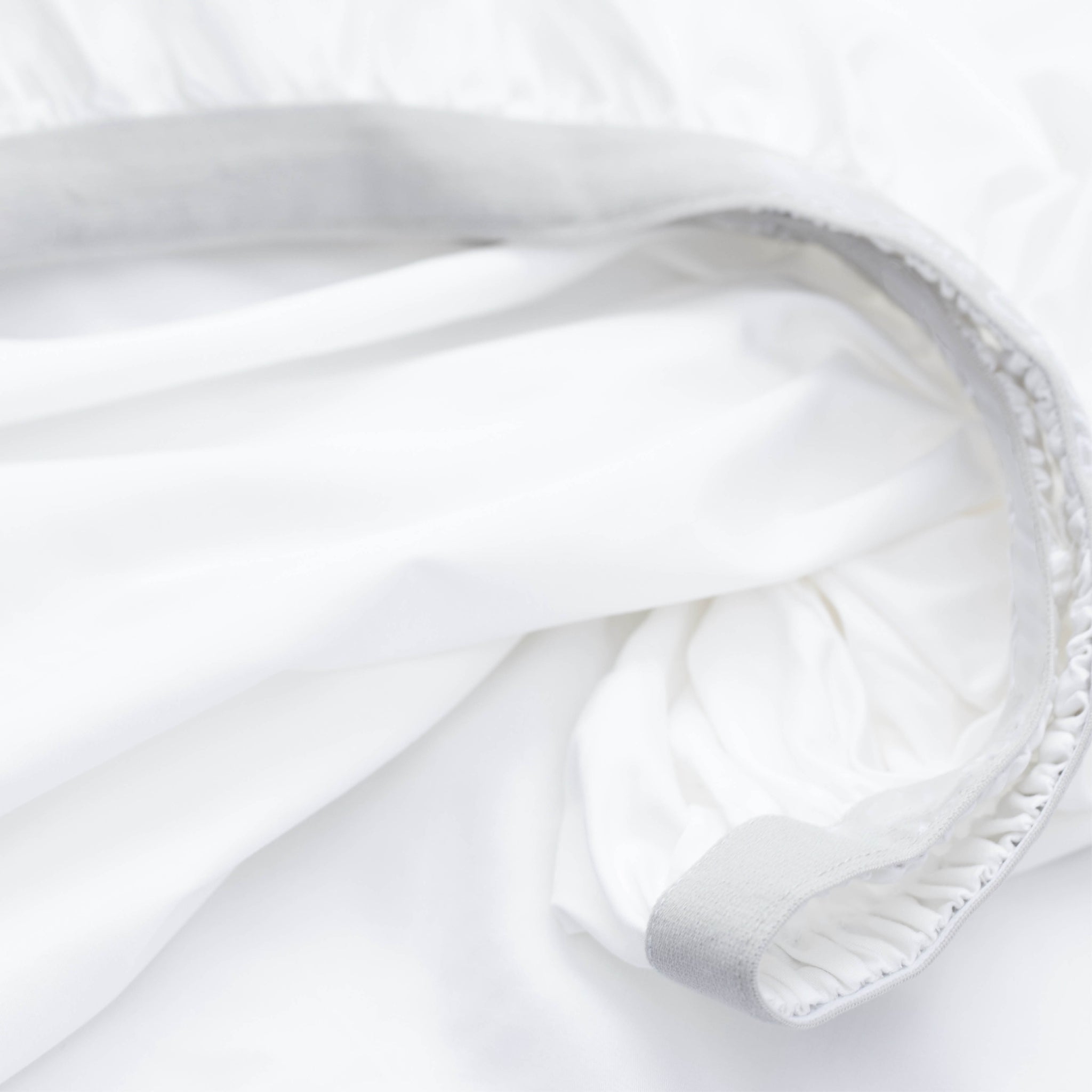 Close-up of a white fitted sheet with a light gray elasticized edge and stitched hem detail.