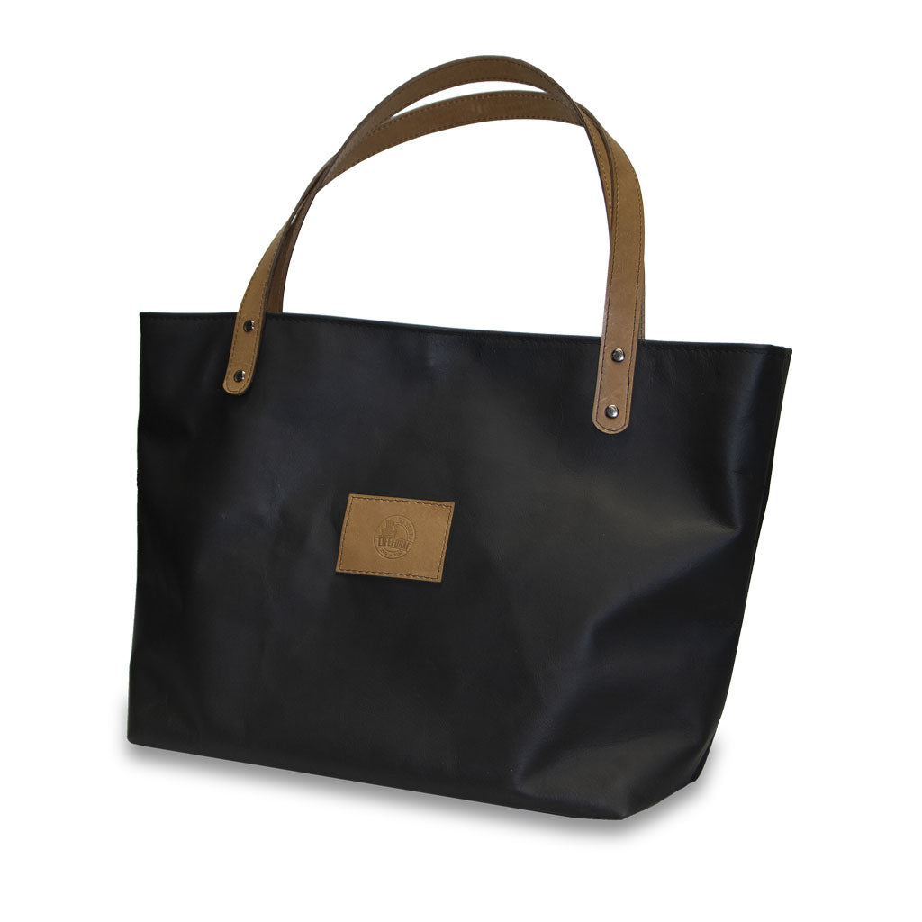Black tote bag with brown leather handles and patch on a white background