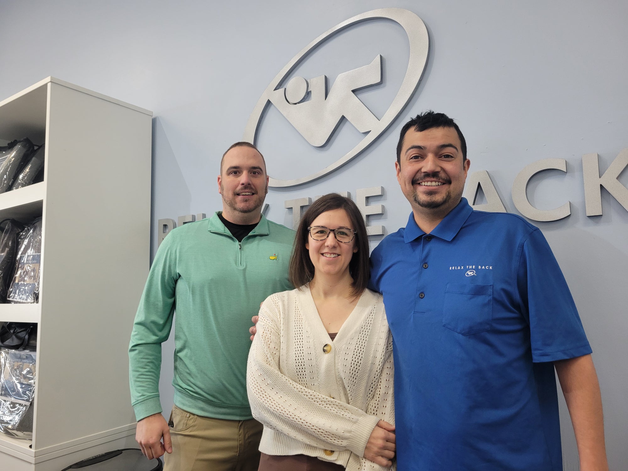 Three people standing in front of a logo on a wall