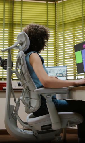 Person using a ergonomic chair at a desk with a computer setup.