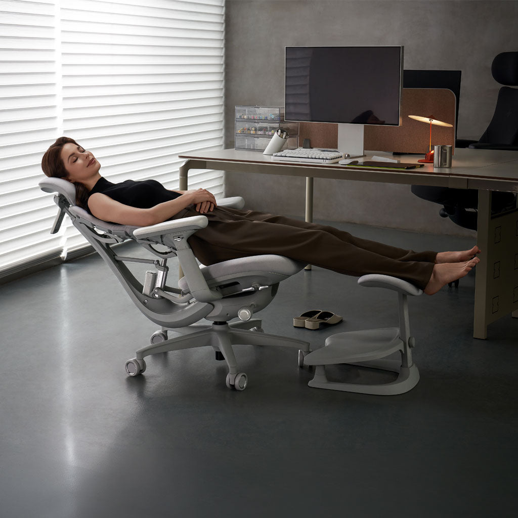 Person lying on a modern office chair in an office setting with a desk and computer.