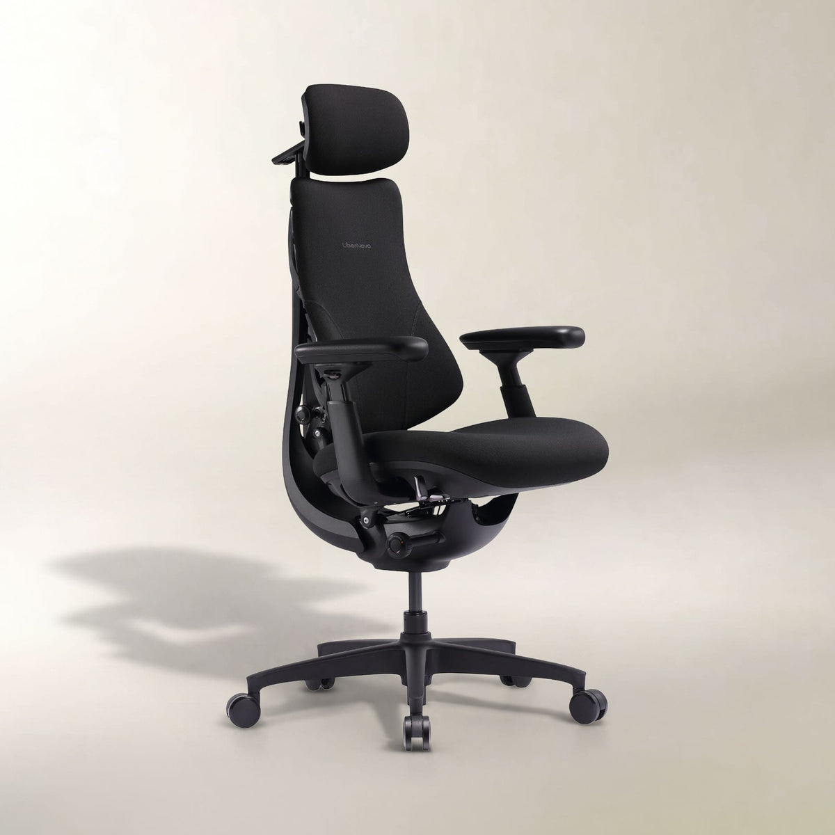 A black ergonomic office chair with a headrest, adjustable armrests, and a five-wheel base, photographed against a neutral light beige studio background.