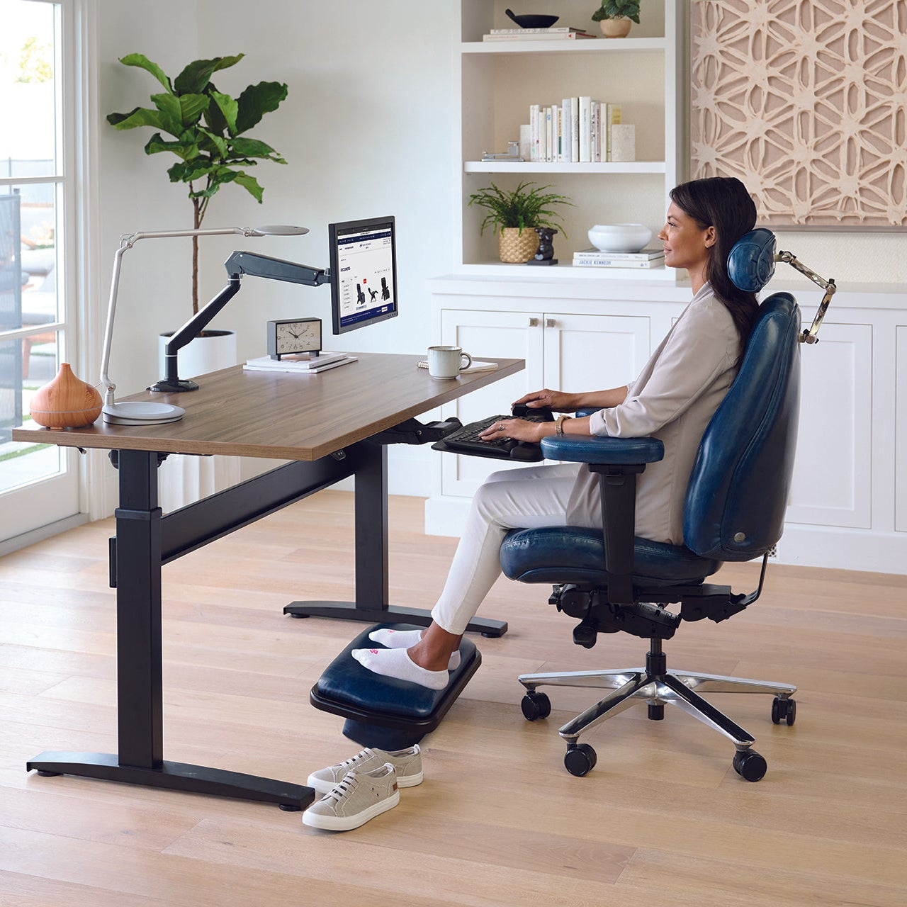 Person using a ergonomic office chair and desk setup in a bright room.