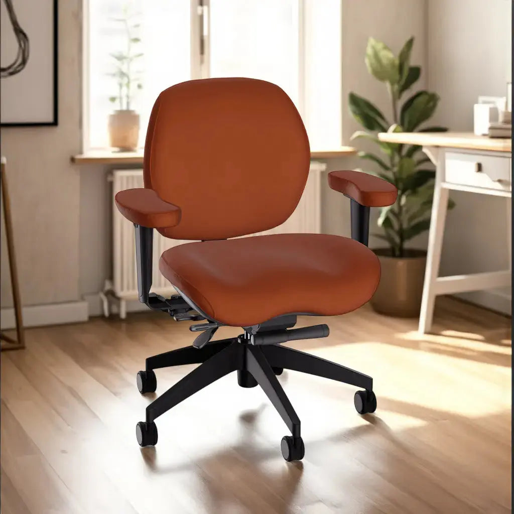 A premium executive office chair upholstered in rich, cognac-colored leather features a wide cushioned seat and backrest, contoured padded armrests, and a black five-star wheeled base. It is shown in a warmly lit home office with wood flooring and natural decor.