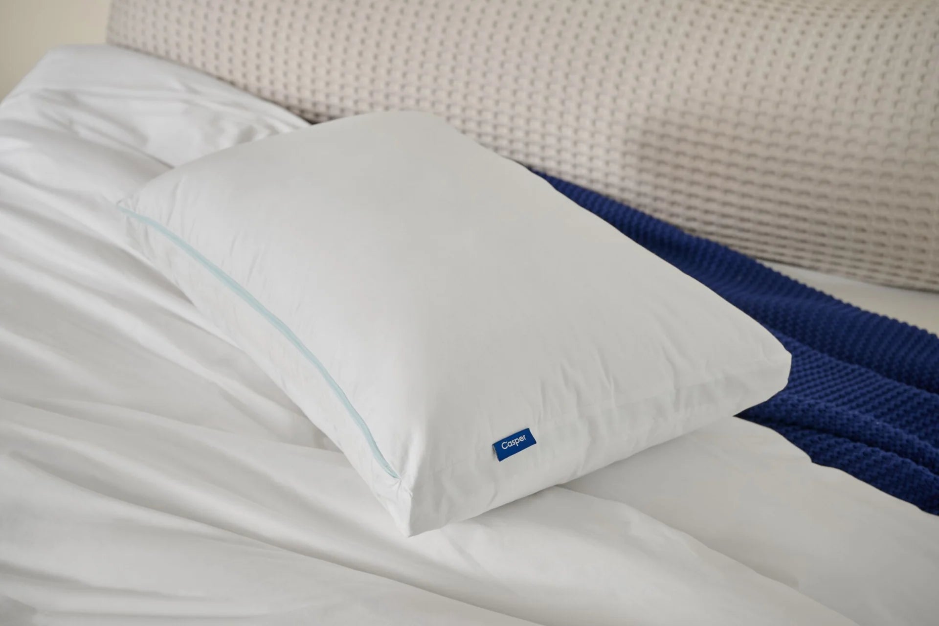 White pillow with a brand logo on a bed with blue blanket