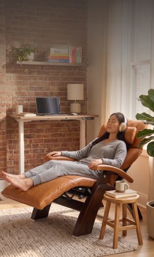 Woman relaxing with her eyes closed in a brown leather recliner in a warm, sunlit home office.