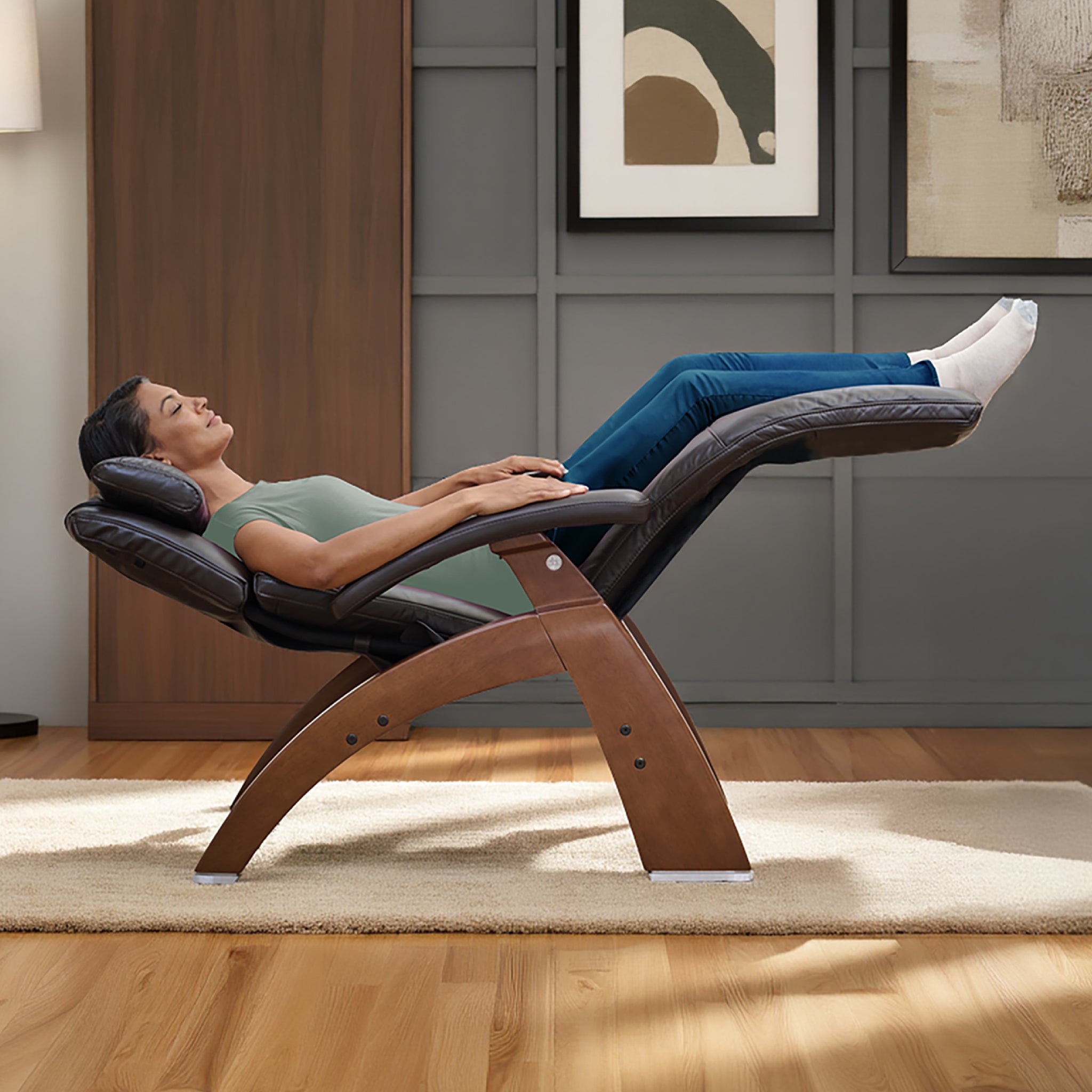 Woman reclining in a zero gravity chair with legs elevated, relaxing in a modern living room with wood flooring and framed artwork on the wall.