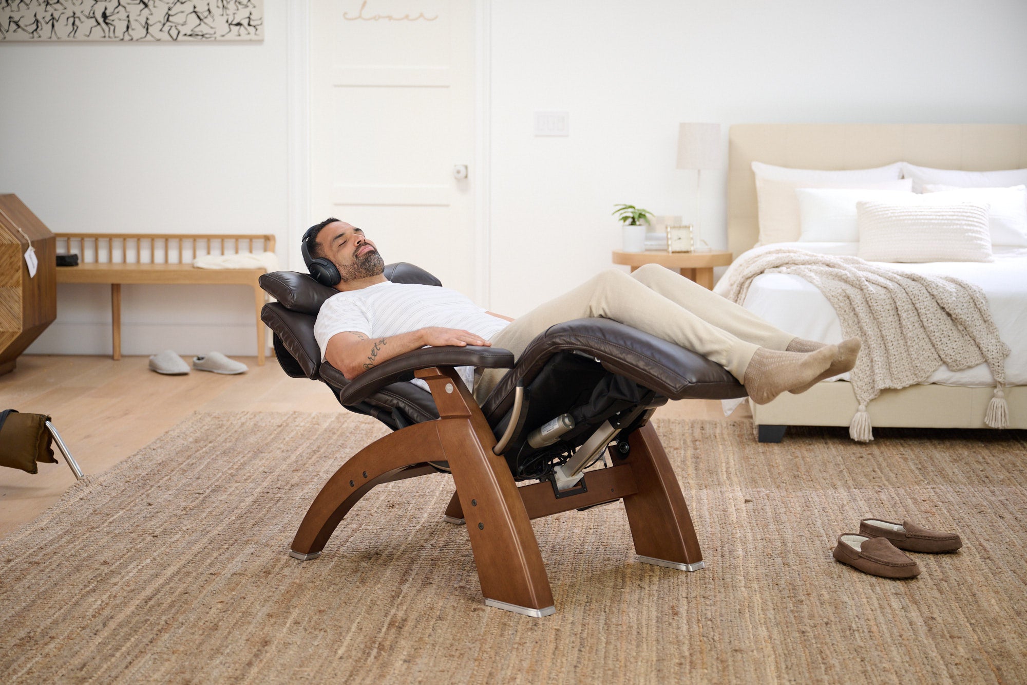 Man relaxing in a wooden recliner chair in a bedroom.