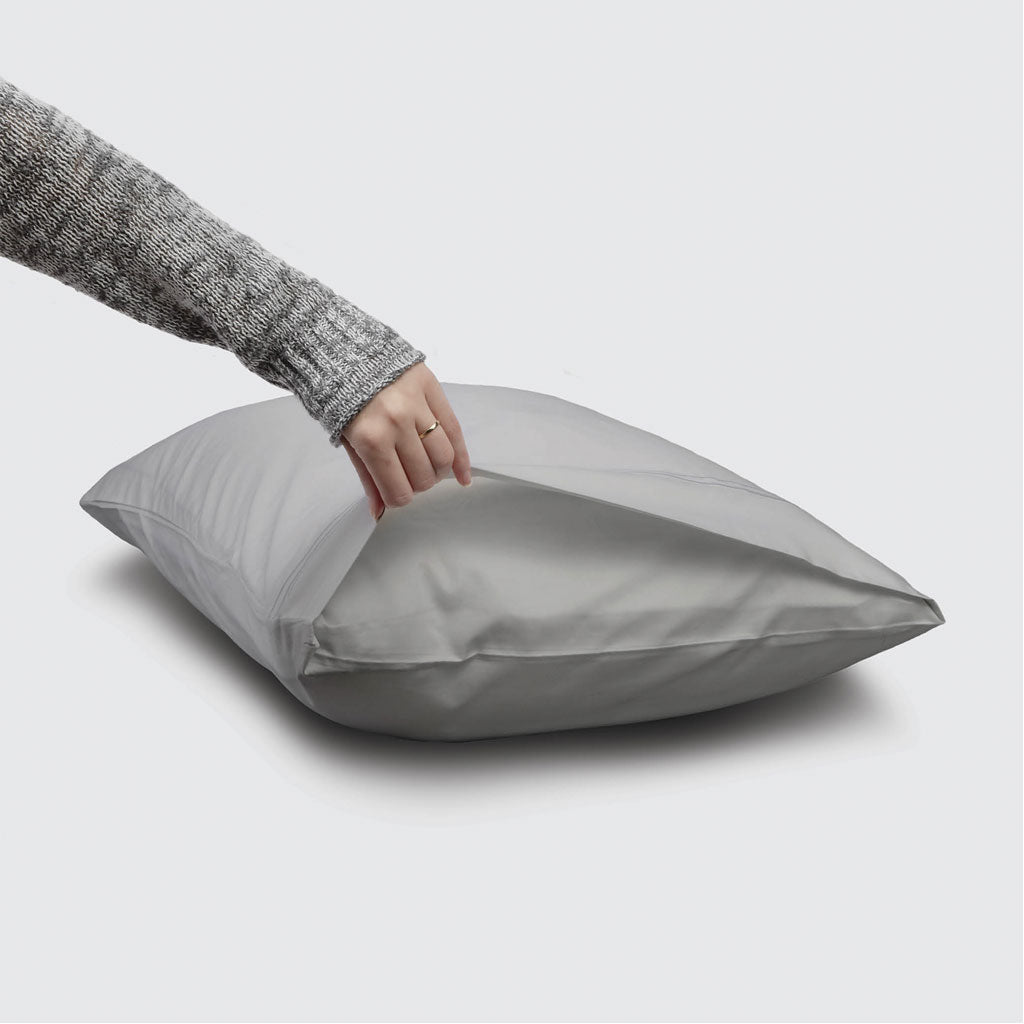 Person holding a gray satin pillowcase on a light gray background