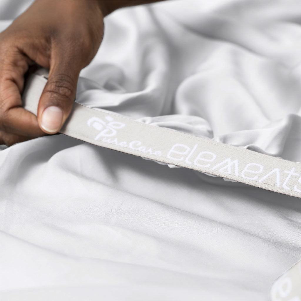 Hand holding a white strap with 'element' branding on a white bed sheet