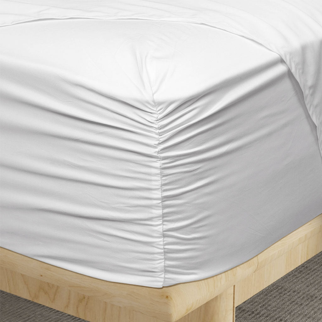 White fitted sheet on a wooden bed frame with a neutral background