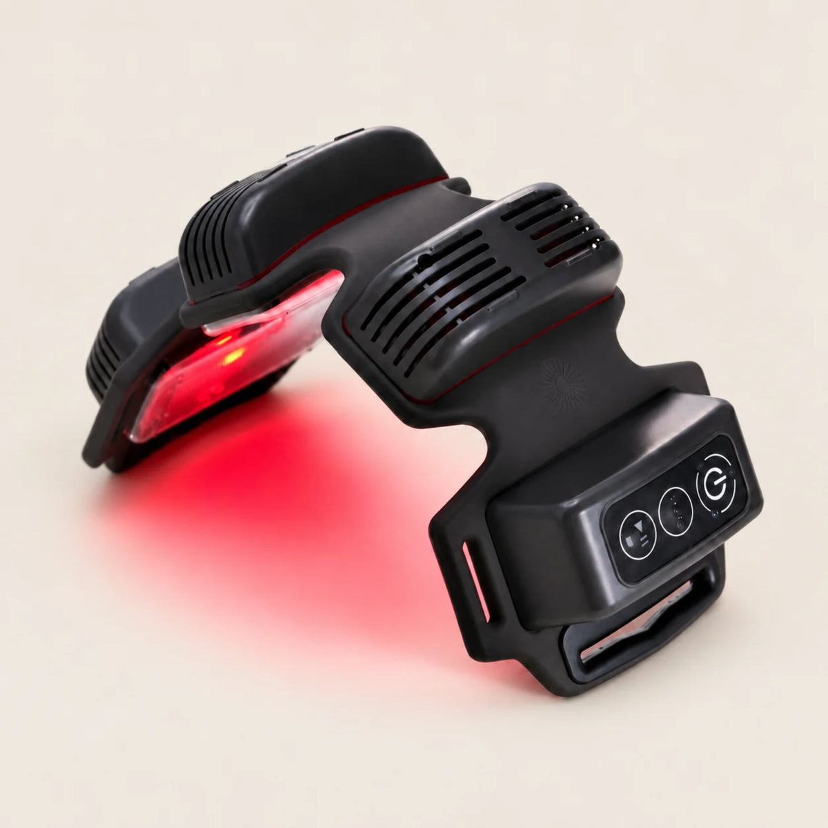 A black wearable red light therapy device with a glowing red light therapy panel, shown on a beige studio background with a red glow.