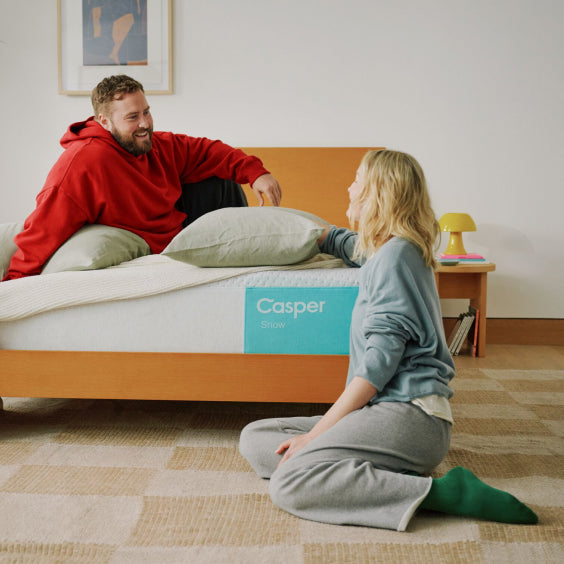 Two people sitting on a Casper mattress in a bedroom.